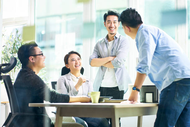 group of four happy young asian corporate people teammates meeting discussing business in office.